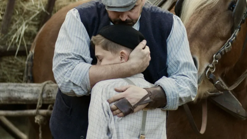 Un homme serre un enfant contre lui devant un cheval et une charrette