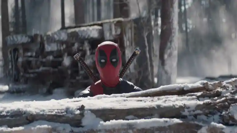 Deadpool en costume rouge derrière des troncs enneigés dans Deadpool & Wolverine