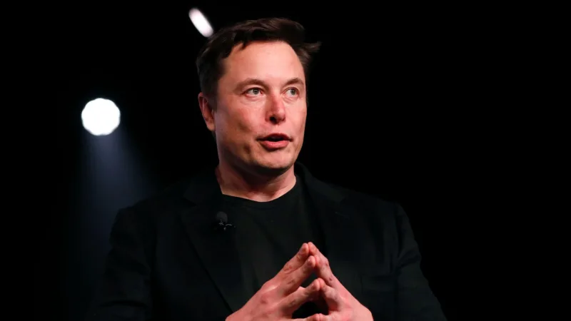 Elon Musk s’exprimant sur scène, vêtu de noir, sous des projecteurs