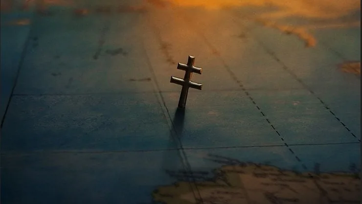 Une Croix de Lorraine se dresse sur une carte ancienne éclairée par le soleil
