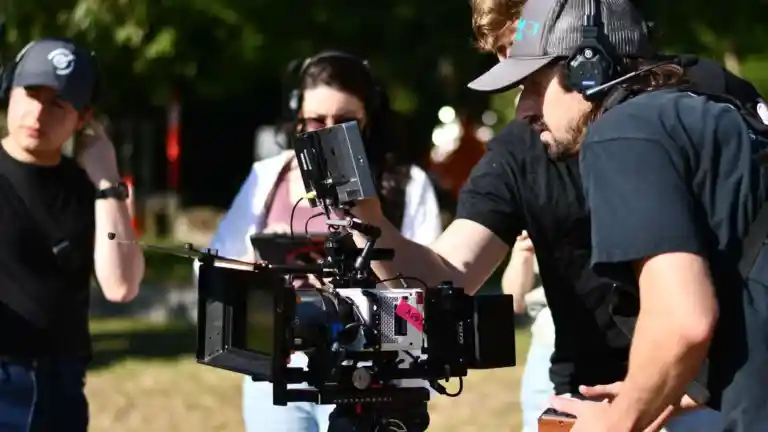 Opérateur réglant une caméra de cinéma entouré de membres de son équipe en extérieur