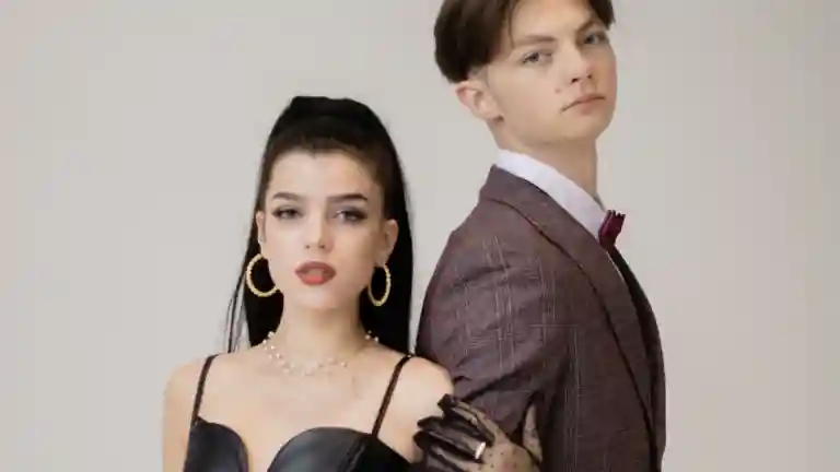 Jeune femme en robe noire et jeune homme en costume brun posant en studio