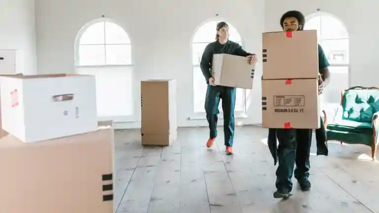 Deux hommes en tenue de déménageur transportent des cartons dans une maison