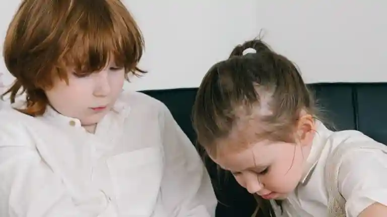 Deux enfants assis côte à côte et concentrés sur leur jeu