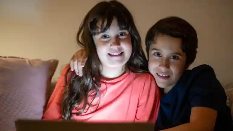 Une fille et un garçon souriants assis côte à côte devant un ordinateur