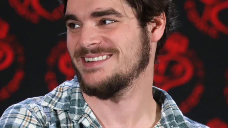RJ Mitte souriant au Rose City Comic Con, Portland, 6 septembre 2024, chemise à carreaux devant un fond sombre