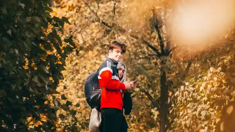 Deux jeunes se tiennent proches dans un parc arboré aux couleurs d'automne