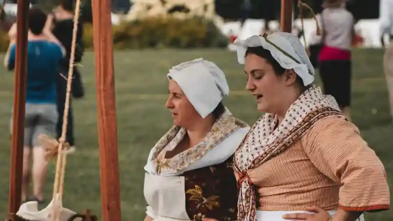 Deux femmes habillées en costumes historiques avec coiffes claires lors d'une reconstitution en plein air