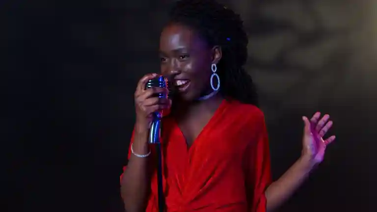 Une chanteuse en robe rouge interprète un morceau au microphone devant un fond sombre.