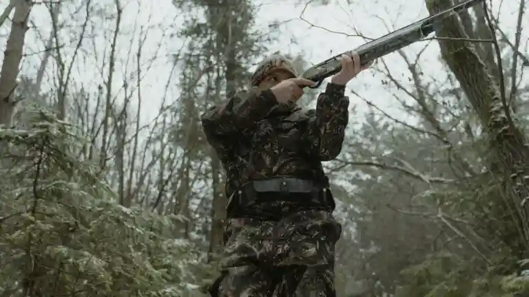 Une personne en tenue de camouflage dans une forêt enneigée, photographie illustrative du métier de chasseur.