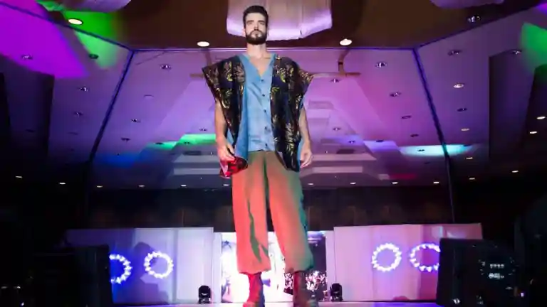 Un mannequin masculin défile sur une scène de mode éclairée en violet