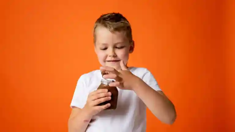 Un garçon en tee-shirt blanc tient un pot de chocolat devant un fond orange
