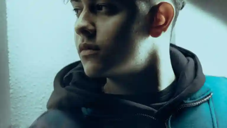 Un jeune homme en sweat sombre regarde vers le côté, photographie illustrative du casting Première fois.