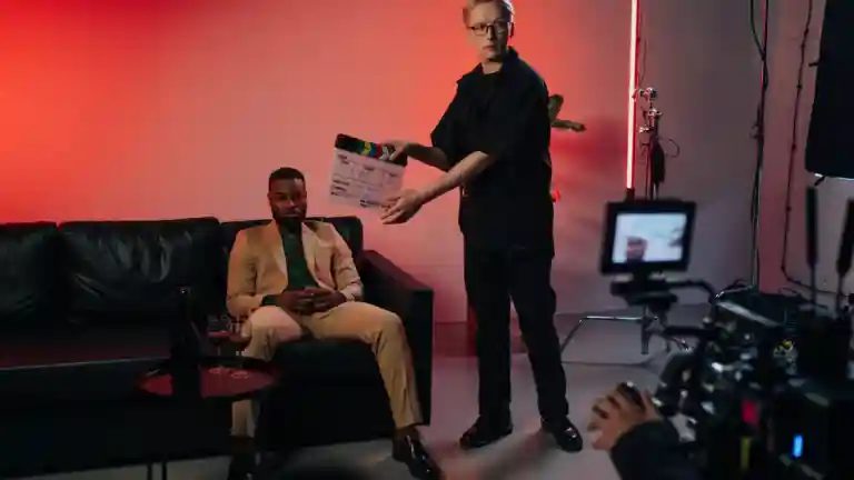 Un homme assis sur un canapé est filmé par une équipe, avec un clap au premier plan.