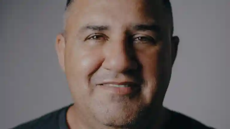 Un homme adulte sourit face à l'objectif sur un fond neutre.