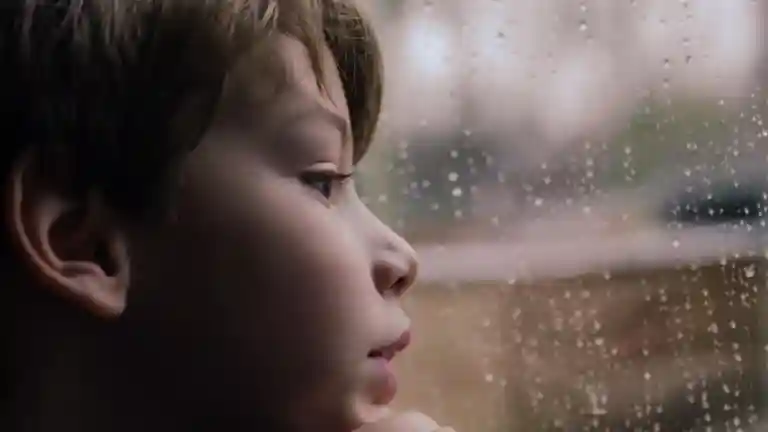 Profil d'un jeune garçon pensif regardant la pluie sur la vitre d'une fenêtre