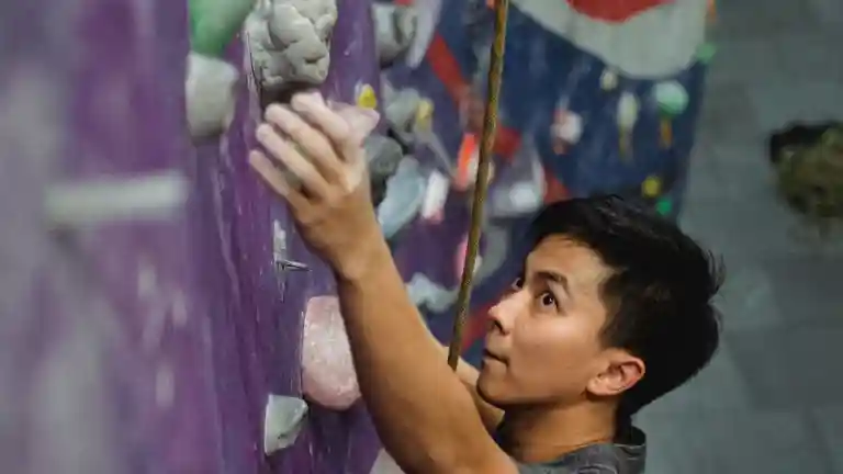 Un jeune homme progresse sur un mur de grimpe en salle