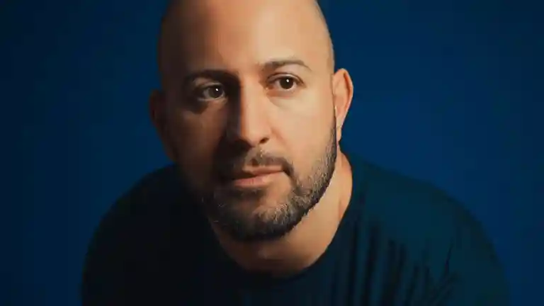 Portrait d’un homme au crâne rasé et à la barbe courte devant un fond bleu