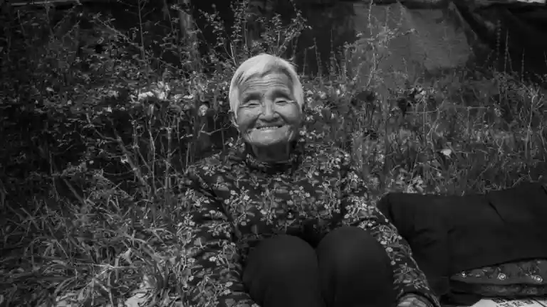 Femme âgée souriante dans un jardin, photographie en noir et blanc
