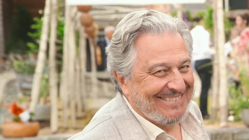 Christian Clavier souriant, cheveux gris et veste beige, portrait en extérieur