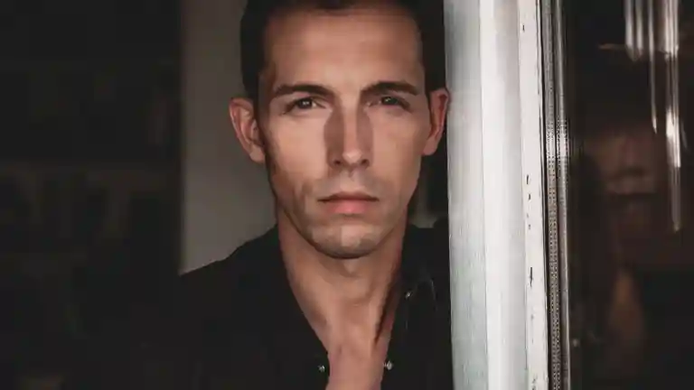 Portrait d'un homme au regard sérieux, près d'une fenêtre