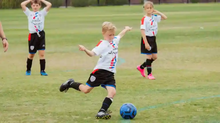 Enfant joueur de football frappant un ballon bleu sur une pelouse