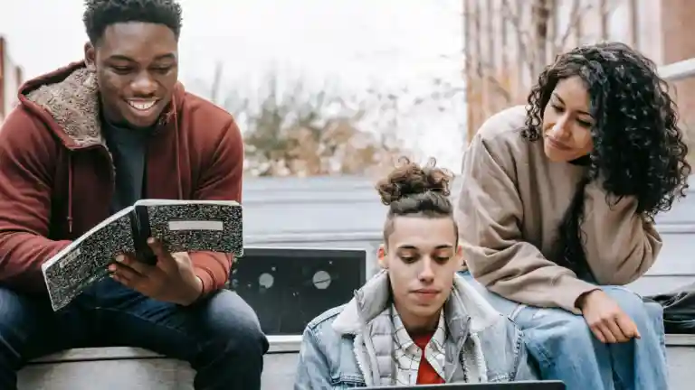 Trois jeunes adultes étudient avec un ordinateur et un cahier en extérieur