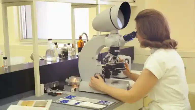 Photographie d’archive de juin 1970 montrant une technicienne en laboratoire devant un microscope