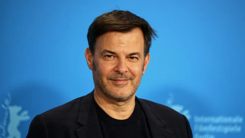 François Ozon en veste noire devant le fond bleu de la Berlinale