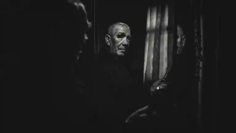 Homme filmé en noir et blanc devant une surface sombre réfléchissante, ambiance de thriller