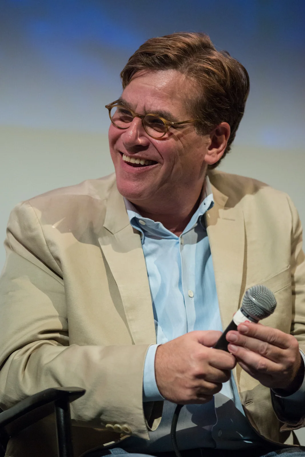 Aaron Sorkin assis avec un microphone, portant une veste claire et des lunettes