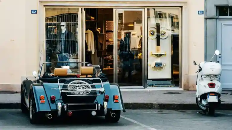 Une voiture décapotable bleue et un scooter blanc stationnés dans une rue de Saint-Tropez